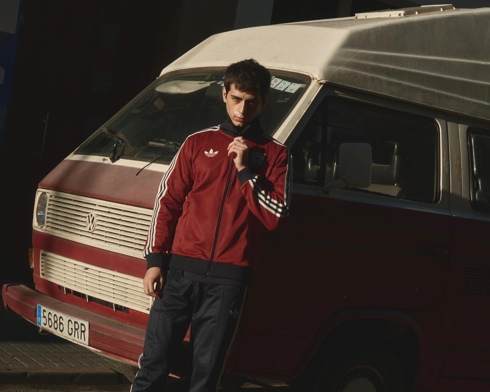 Modelo con chaqueta Adidas granate apoyado en una furgoneta antigua