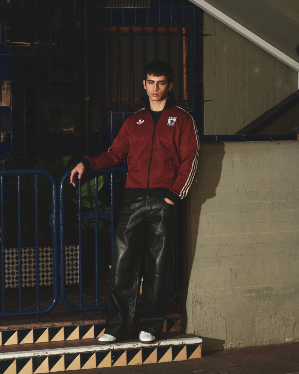 Modelo con chaqueta Adidas granate y pantalón de cuero junto a una valla azul