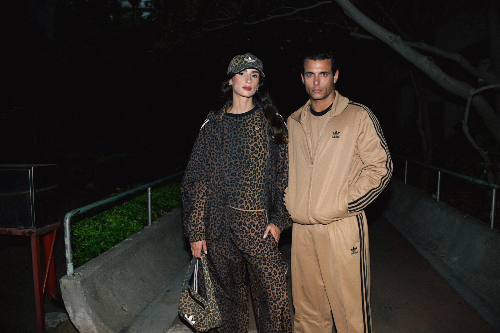 Dos modelos de noche en un parque: ella con un conjunto Adidas de estampado de leopardo y él con un chándal beige