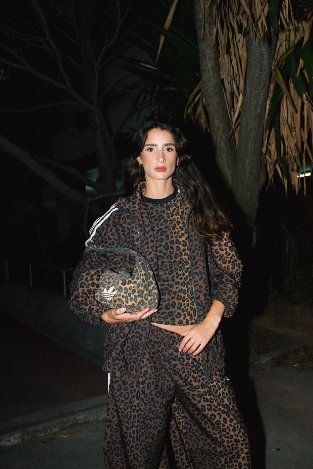 Modelo con conjunto Adidas de estampado de leopardo y bolso a juego, de noche entre árboles