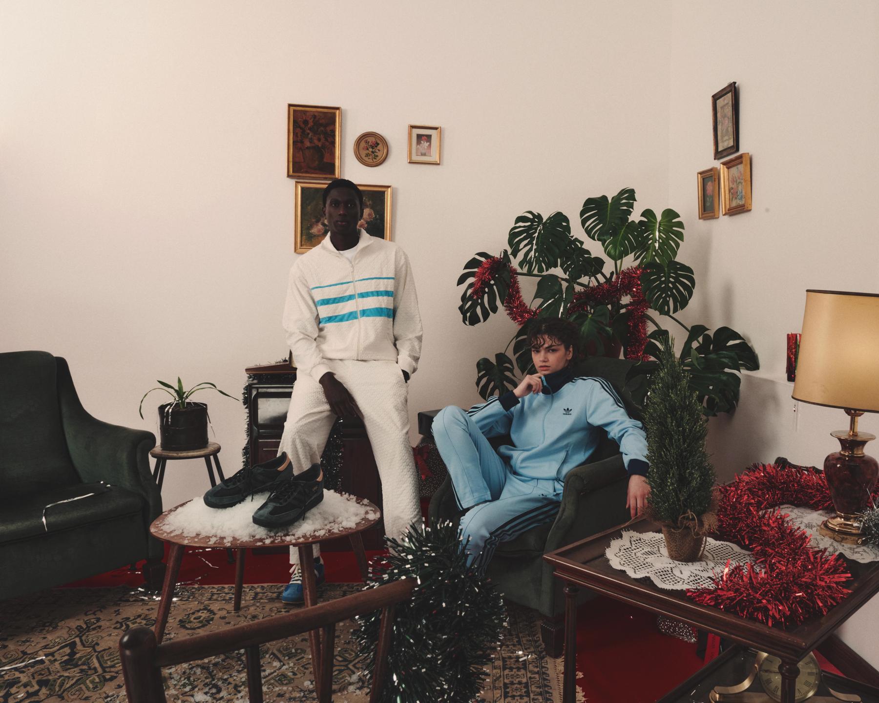 Dos modelos con chándales Adidas en un salón clásico decorado con espumillón y plantas