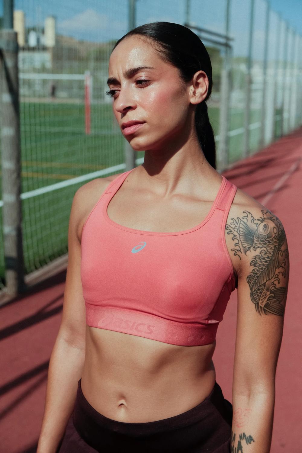 Retrato de una corredora con top deportivo rosa junto a una pista de atletismo
