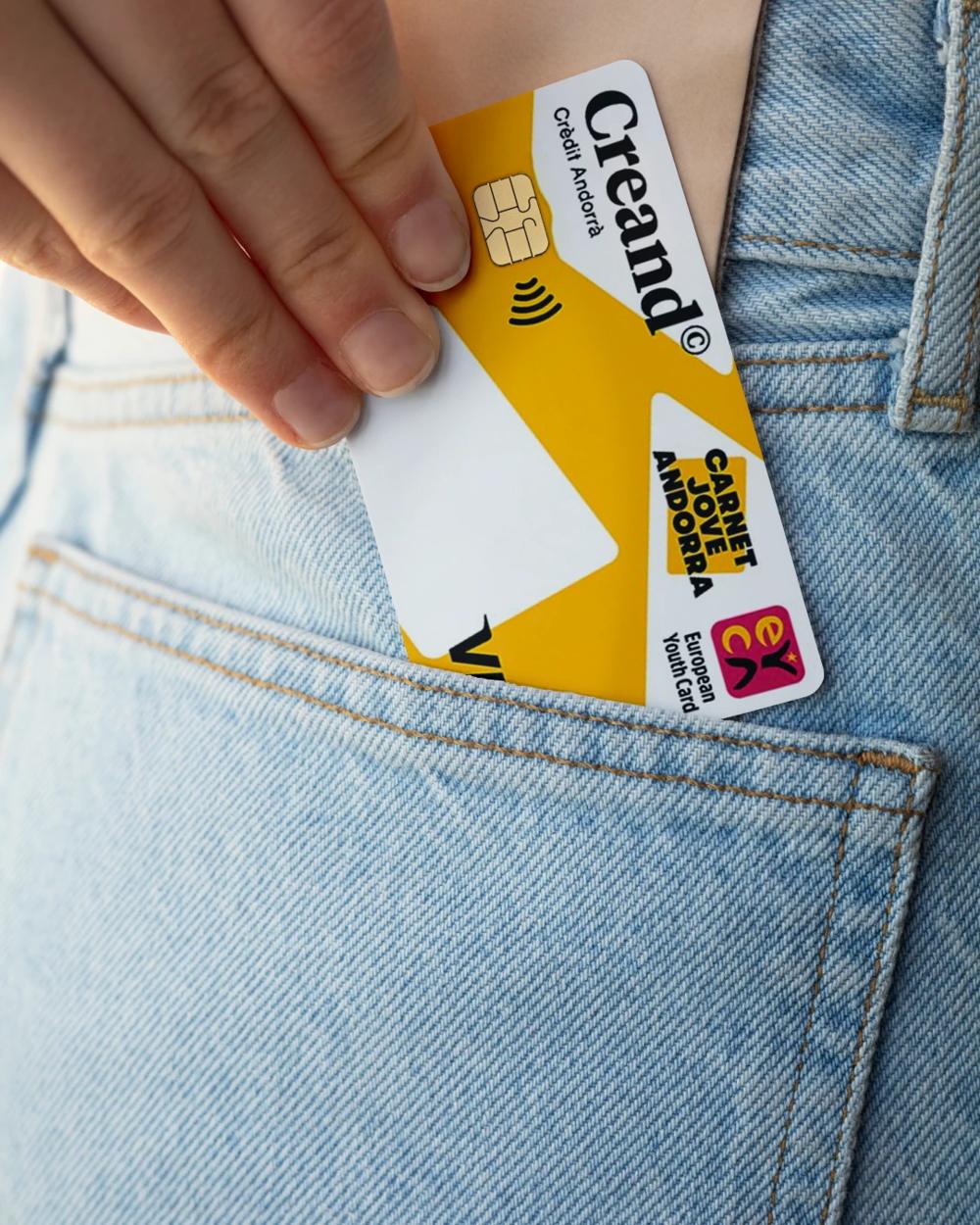Una mano guarda una tarjeta Creand Carnet Jove en el bolsillo de unos vaqueros