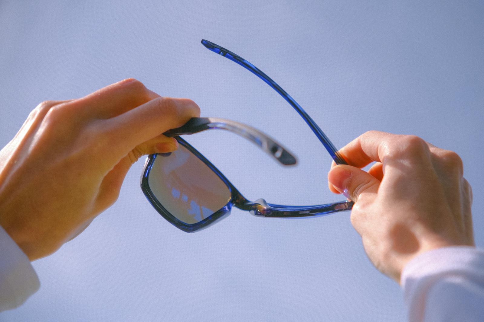 Dos manos doblan unas gafas de sol contra el cielo